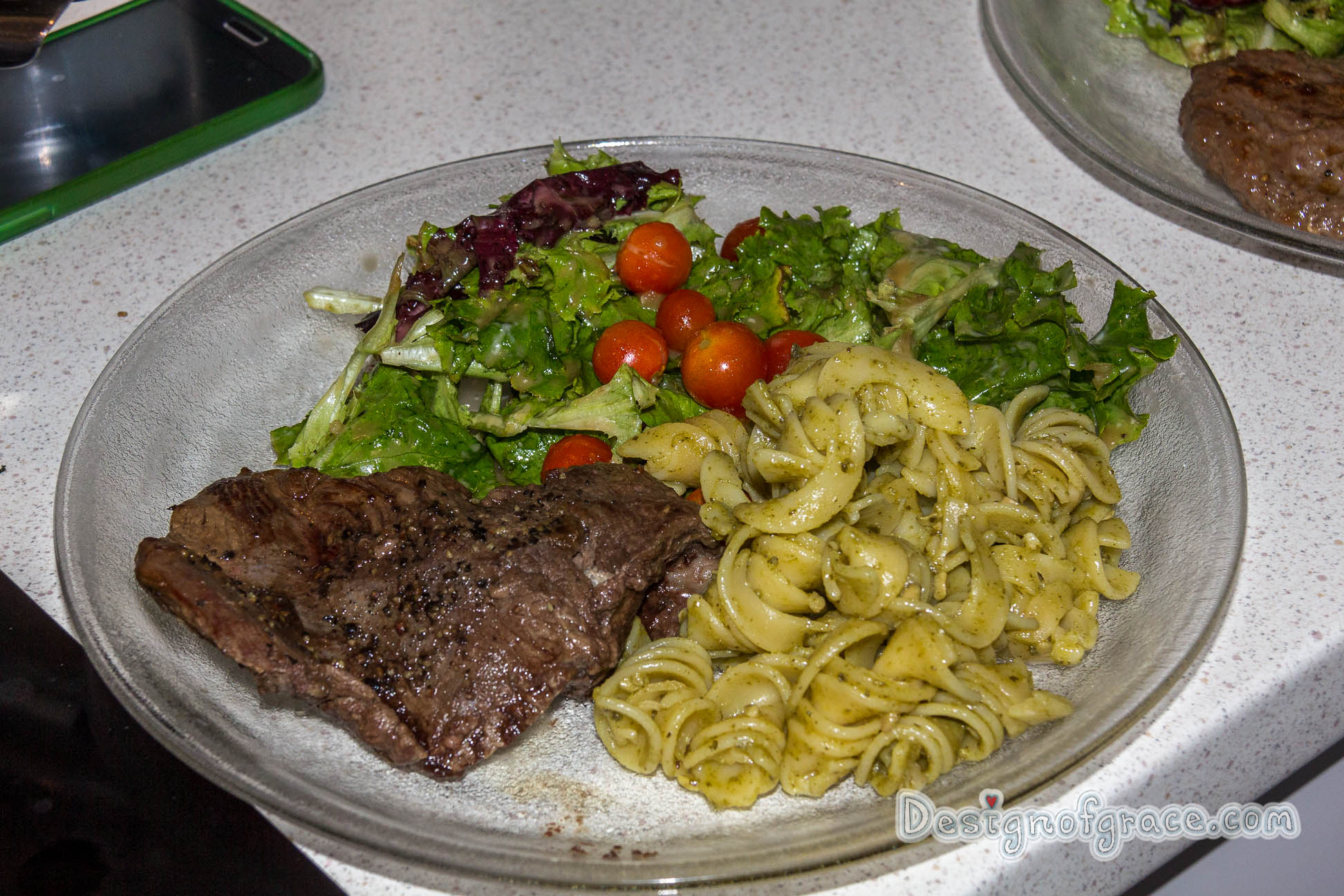 a plate of food with a kangaroo steak on the left which has been nicely browned with pesto pasta on the right and the home grown green and red lettuce and cherry tomatoes on top of the plate