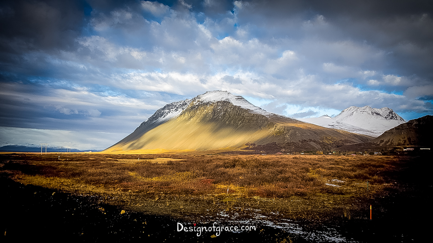 A lone snow capped mountain with interesting sun pattern on it and dramatic clouds