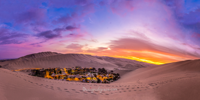 Blue, orange and purple skiles at sunset with the city of huacachina with lights lit up