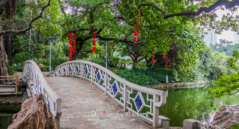 Liwan Lake Park bridge with green trees and red lanterns hanging from the trees with the lake on the right, Guangzhou, China
