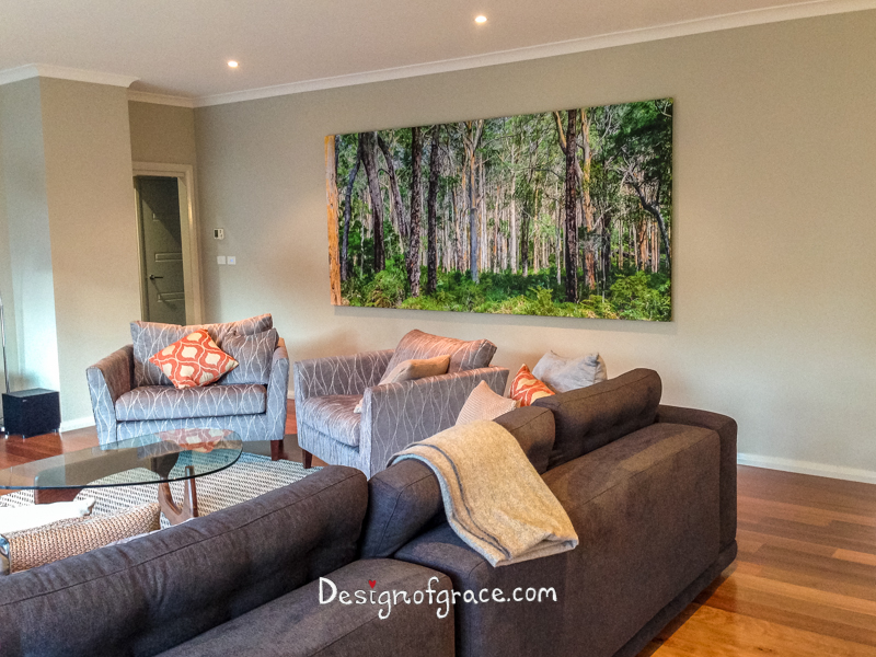 A photo of my client's living room with grey couch and orange and white pillows with the 3 x1.4m canvas print of the green and gray Karri Forest