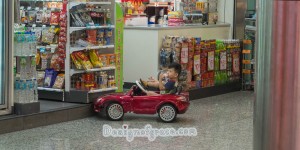 A little boy in a cool red toy car outside a shop
