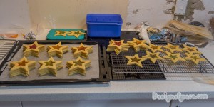 An overview of the two tray of baked star cookies with the middle hollowed out in a star shape filled with colouful lollies baked