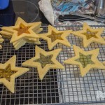 A tray of baked star cookies with the middle hollowed out in a star shape filled with colouful lollies baked