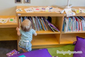 A baby using the bookshelf to stand up to reach the finished buntings