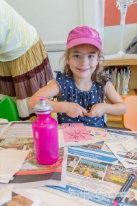 a smiley girl in a pink cap while trying to cap her marker