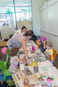 A table in middle with kids on either side and adults supervising the workshop