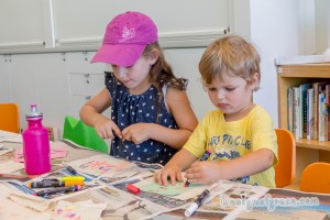 a girl with a pink cap on the left and a boy in a yellow shirt both busy drawing on their bunting