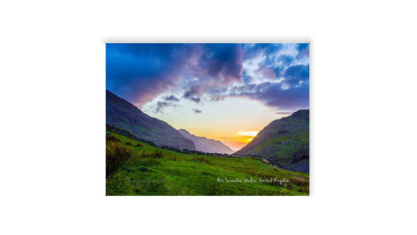 Snowdon Valley Sunset with purple and orange hues contrasted with the green grass on the bottom with 2 mountain on either side with the sun in the setted in the middle, Wales, UK